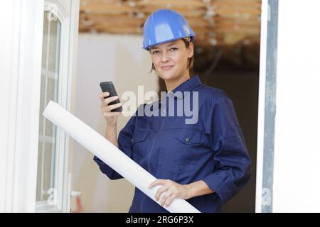 architect in helmet with paper documents holding her phone Stock Photo