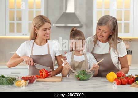 Three generations. Happy grandmother, her daughter and granddaughter cooking together in kitchen Stock Photo