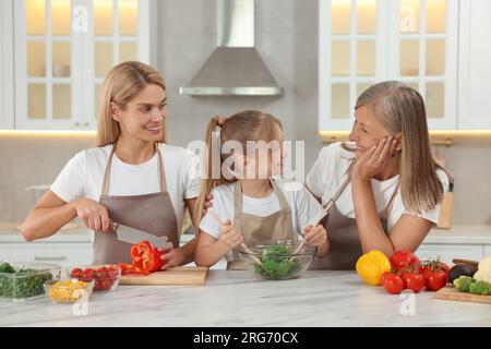 Three generations. Happy grandmother, her daughter and granddaughter cooking together in kitchen Stock Photo