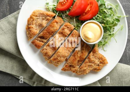 Tasty cut schnitzel served with sauce, microgreens and tomato on grey table, top view Stock Photo