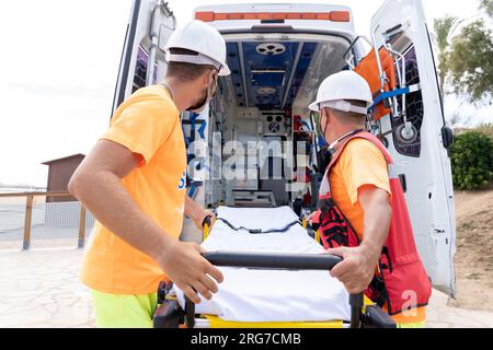 Rear view of two lifeguards taking a stretcher out of ambulance on the beach Stock Photo