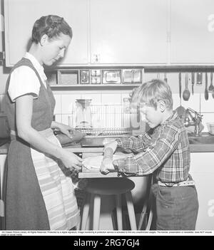 Baking in the 1950s. A mother with her son in the kitchen. He helps her with the baking, rolling the dough on an extendable bench board.  Sweden 1958 Kristoffersson ref BY18-11 Stock Photo