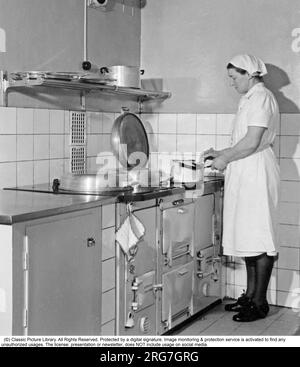 The AGA cooker. A swedish invention by Gustaf Dalén with the principle of heat storage, a combination of two large hotplates and two ovens into one unit, the AGA cooker. The oldest AGA cooker still in use belongs to the Hett family of Sussex and it was installed 1932. This picture was taken 1950 where a woman is seen cooking something on the stove. Sweden Stock Photo