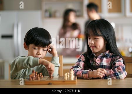 two asian children brother and sister sitting at table at home playing chess Stock Photo