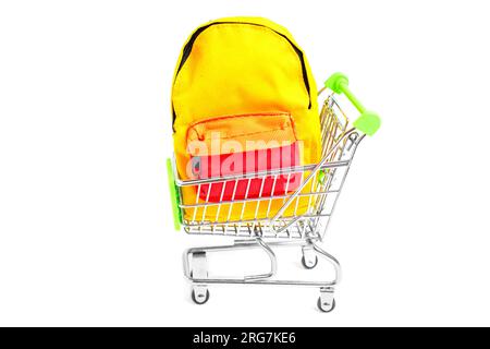 Small vibrant backpack placed inside a miniature shopping trolley isolated on white background with copy space. Creative back-to-school concept. Stock Photo