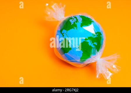Miniature globe model wrapped in plastic, resembling a candy. Plastic pollution and waste related background with copy space. Stock Photo