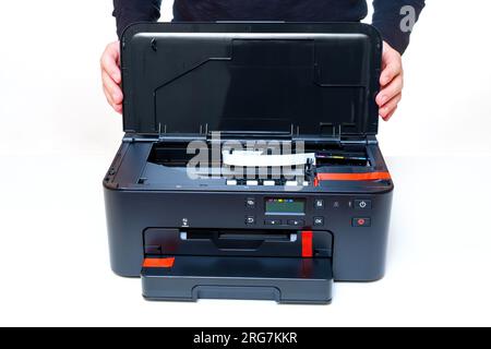 Person holds onto the open lid of a brand-new printer, placed on a clean white table. Completeness and condition inspection. Stock Photo