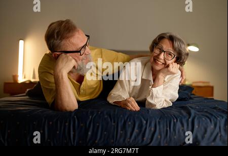 Portrait of excited senior married couple lying on bed and laughing Stock Photo