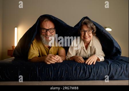 Portrait of smiling senior family couple in bed lying under blanket Stock Photo