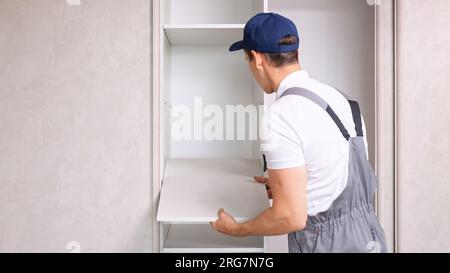 Male worker assembles light wardrobe attaching shelves Stock Photo