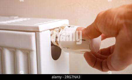 Man hand regulates temperature on radiator in premise Stock Photo