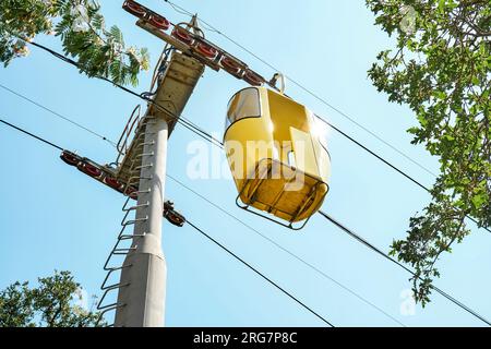 Yellow cabin of overhead cable car against sunlit blue sky. Touristic attraction in amusement park for arrived visitors at resort Stock Photo
