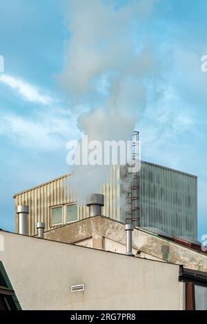 Industrial chimney fume and steam exhaustion on old factory building, selective focus Stock Photo