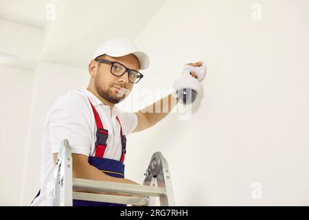 Portrait of maintenance worker adjusting wall-mounted dome surveillance camera inside house. Stock Photo