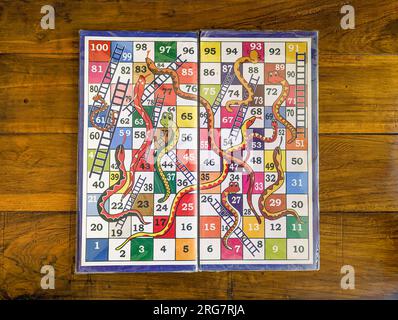 closeup of a colorful version of a snake and ladders multiplayer board game in a wooden table background Stock Photo