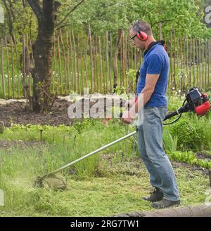 Worker mowing tall grass with electric or petrol lawn trimmer Stock Photo