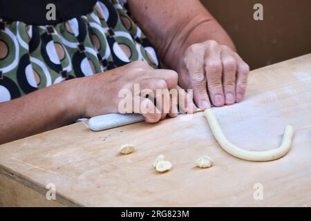 Close up on the hands of a woman preparing orecchiette, the typical apulian pasta, on the street in downtown in Bari Stock Photo