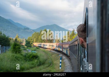 Man traveling by railway through Balkans. Handsome young guy looking out the train window. Tourist male traveller looking out from sleeping car wagon Stock Photo