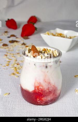 Delicious and healthy still life of yogurt and muesli, with strawberries in the background. Contrast colors. Vertical view. Stock Photo