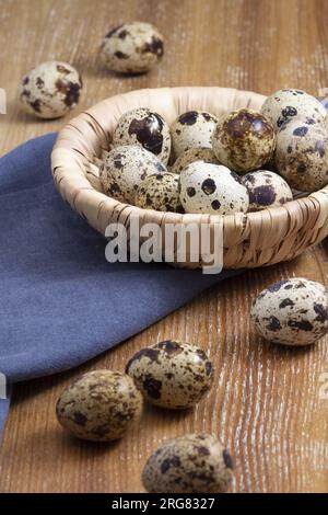 Still life of a few quail eggs in a little basket on a wooden background. Vertical view. Stock Photo
