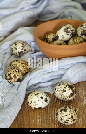 Still life of a few quail eggs in a little clay bowl on a wooden background. Vertical view. Stock Photo
