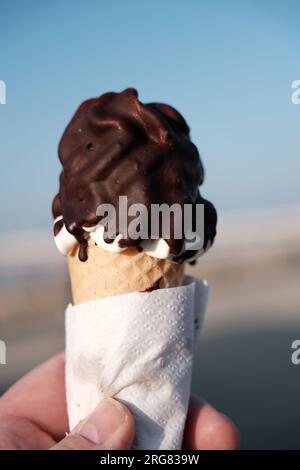 Creamy chocolate ice cream cone, held temptingly close-up in a hand. Stock Photo