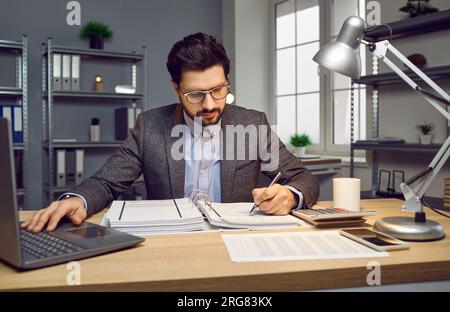 Portrait of focused businessman sitting at desk with laptop computer Stock Photo