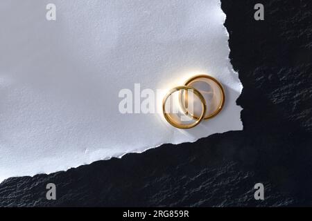 Macro of white textured paper card with two engagement rings on slate base table. Top view. Stock Photo