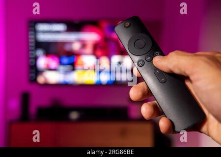 remote control in hand with tv in background. streaming service, content on demand. watching online television at home Stock Photo