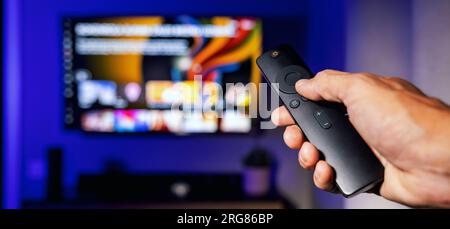 remote control in hand with tv in background at home. streaming service, content on demand. banner with copy space Stock Photo