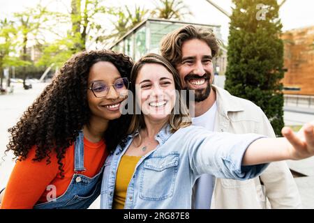 Diverse group of three friends taking a selfie in the street. Cheerful multiracial group of young hipsters taking a picture outside. Stock Photo