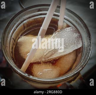 close up of iced tea and ice cubes in a glass cup with a plastic straw Stock Photo