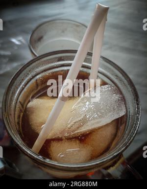 close up of iced tea and ice cubes in a glass cup with a plastic straw Stock Photo