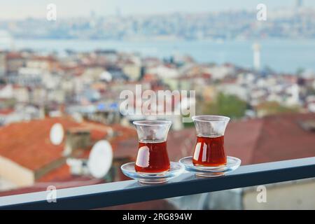 Two Turkish glasses in form of a tulip filled with hot black tea with view to the roofs of Uskudar district on Asian side of Istanbul, Turkey Stock Photo