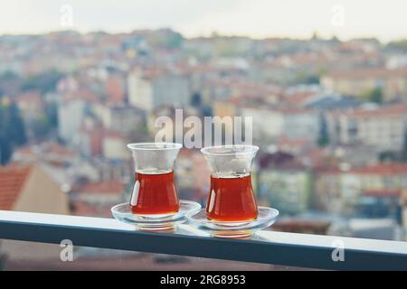 Two Turkish glasses in form of a tulip filled with hot black tea with view to the roofs of Uskudar district on Asian side of Istanbul, Turkey Stock Photo