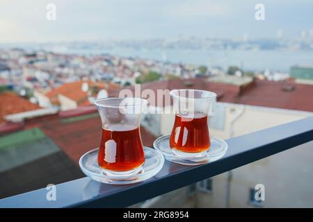 Two Turkish glasses in form of a tulip filled with hot black tea with view to the roofs of Uskudar district on Asian side of Istanbul, Turkey Stock Photo