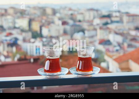 Two Turkish glasses in form of a tulip filled with hot black tea with view to the roofs of Uskudar district on Asian side of Istanbul, Turkey Stock Photo