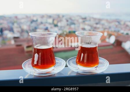 Two Turkish glasses in form of a tulip filled with hot black tea with view to the roofs of Uskudar district on Asian side of Istanbul, Turkey Stock Photo