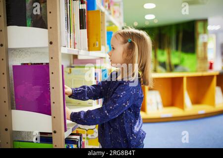 4 year old girl selecting a book in municipal library. Reading and learning concept Stock Photo