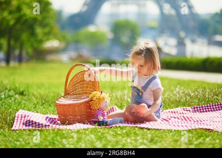 Cheerful toddler girl having picnic near the Eiffel tower in Paris, France. Happy child playing with toys in park on a summer day. Kid enjoying health Stock Photo