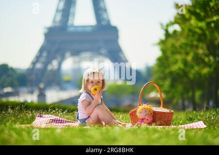 Cheerful toddler girl having picnic near the Eiffel tower in Paris, France. Happy child playing with toys in park on a summer day. Kid enjoying health Stock Photo