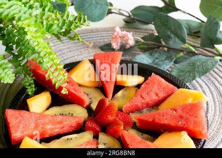 Freshly cut summer fruits arranged on a black plate, creating a vibrant and healthy snack or dessert Stock Photo