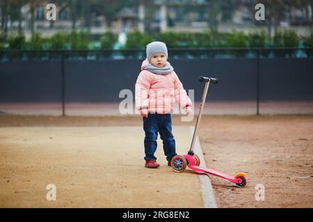 Adorable toddler girl learning how to use kick scooter in park, Paris, France Stock Photo