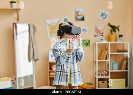 Schoolboy in casualwear and vr headset standing in front of camera in home environment and playing new game while enjoying leisure Stock Photo