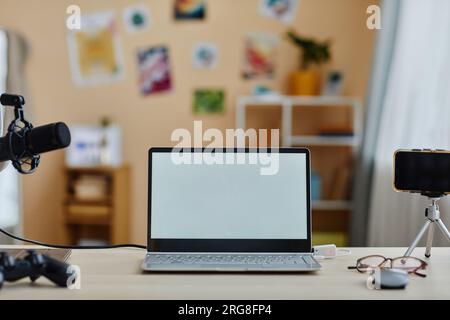 Laptop with blank screen standing on desk among smartphone on tripod and microphone prepared by blogger for livestream or recording podcast Stock Photo