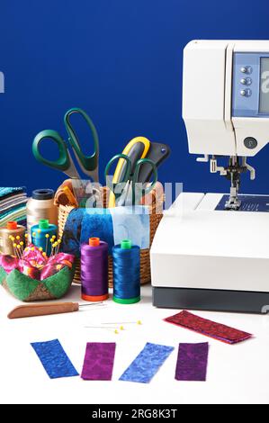 Sewing accessories in a basket and spools of threads next to sewing machine Stock Photo