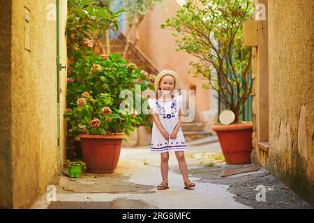 Adorable preschooler girl in white dress and straw hat on a street of Bonnieux village in Provence, France Stock Photo