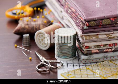 Stack of fabric for patchwork on craft mat, sewing accessories on wooden surface Stock Photo