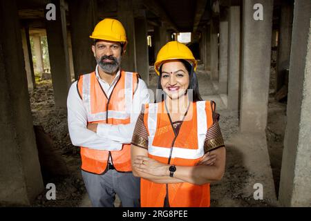 Portrait of two Indian male and female civil engineers or architect wearing helmet standing with cross arms. Real estate. Stock Photo