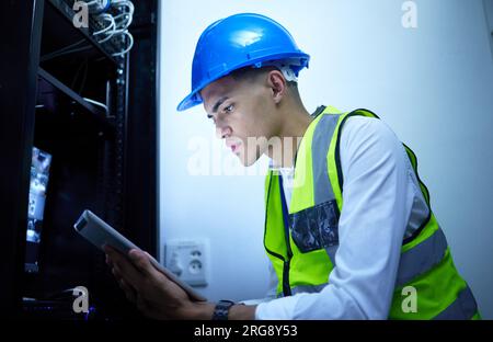 Man, electrician and tablet for power maintenance, server room or data center upgrade in IT or cybersecurity. Young, engineering person on digital Stock Photo